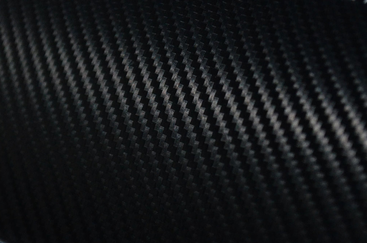 Close-up of a black carbon fiber textured panel with white stitching detail.